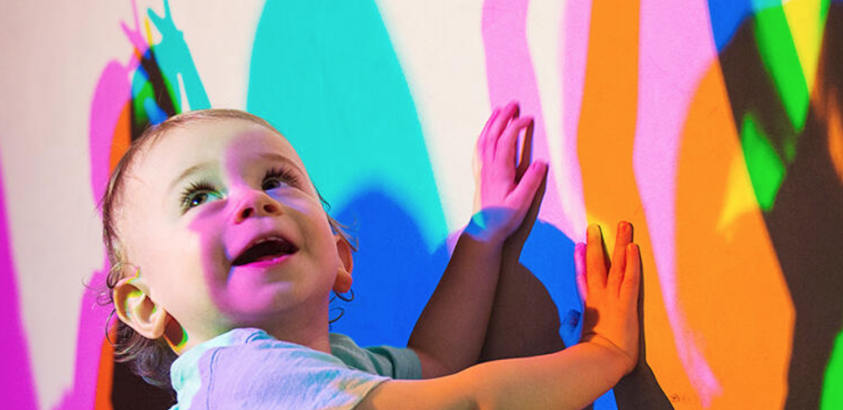 A happy baby playing with colorful shadows at the Exploratorium, photo credit to Exploratorium