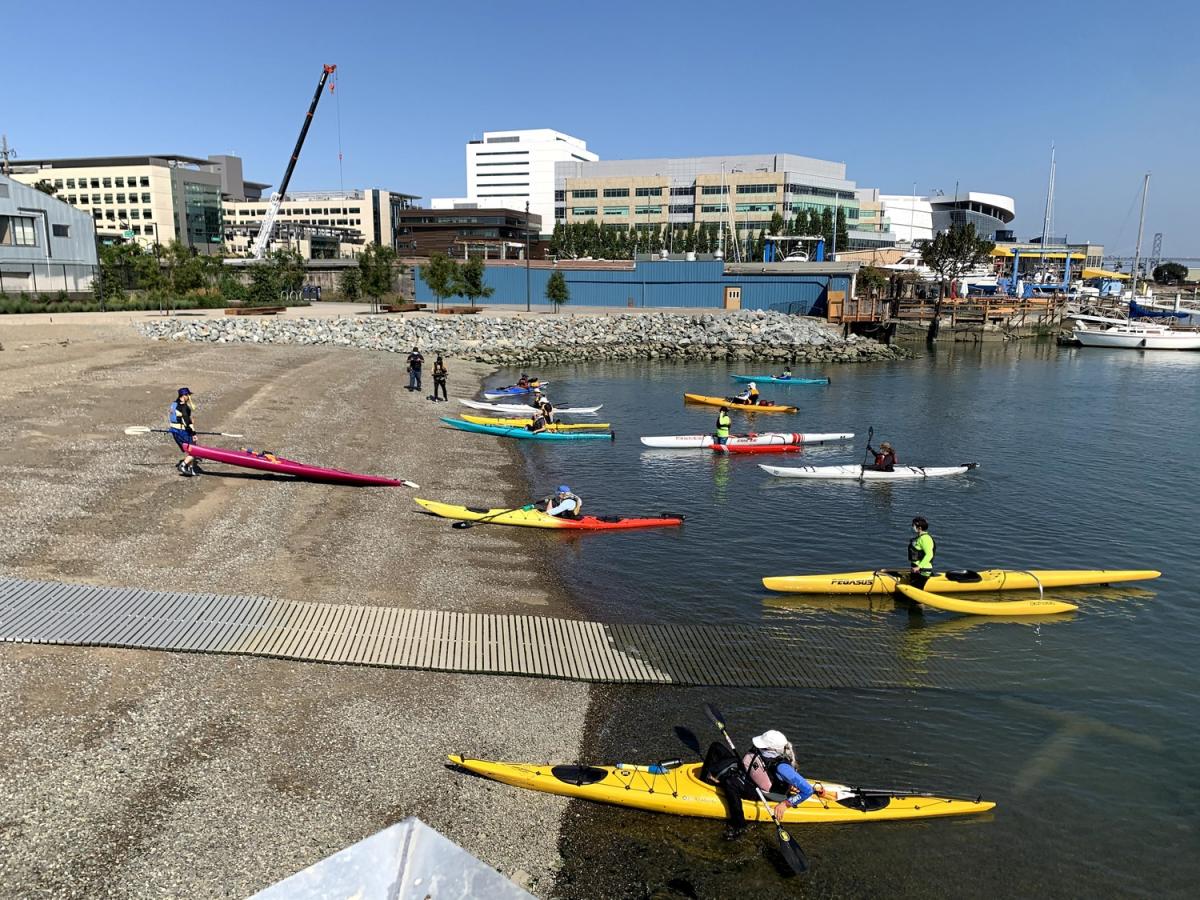 Colorful kayaks prepare to paddle into the open water at the beach at Crane Cove Park.